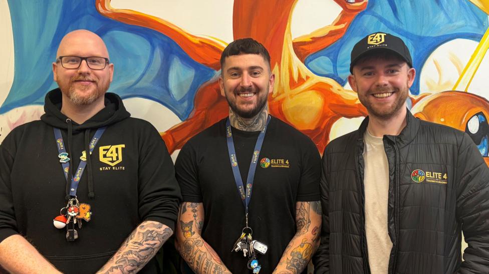 Three men standing infront of a painting of a Pokémon