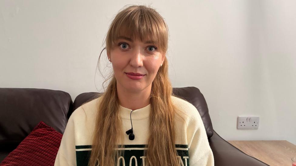 Yana Osibchuk sits on a sofa wearing a cream sweatshirt and looking directly into the camera