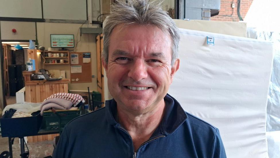 A man wearing a blue jumper smiles into the camera