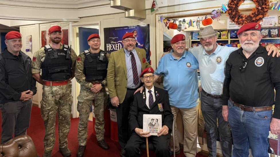 Men in military uniform and red berets are seen lined up, smiling at the camera