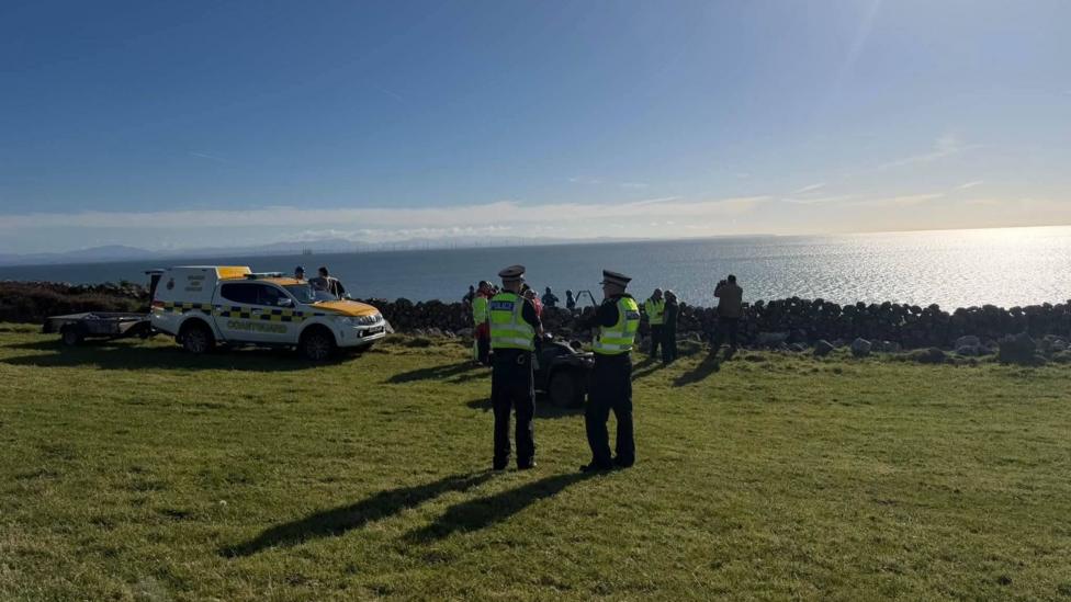 A scene next to a drystane dyke looking out over the Solway with police officers and a coastguard vehicle