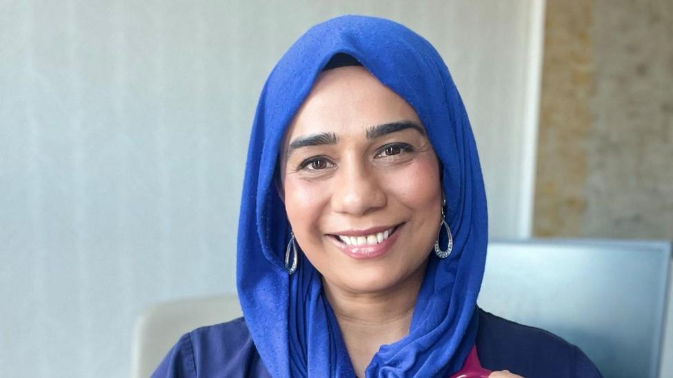 Dr Nighat Arif smiling wearing a blue head dress and hoop earrings