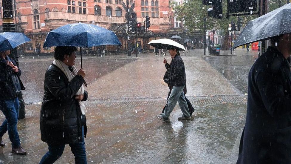 People walking along a street lined with shops with umbreallas in the heavy rain