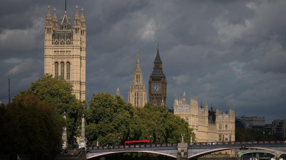A red double-decker bus drives on a bridge in near the Houses of Parliament in London.