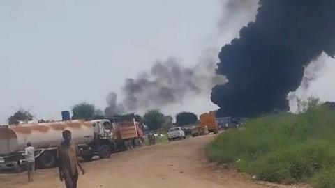 A screengrab from a video on TikTok verified by the BBC taken 600m from Amiet Market showing a dirt road with a petrol tanker and some vehicles and a plume of black smoke in the distance.