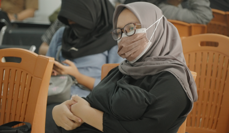 A woman wearing a mask to protect herself from th air pollution waits in a hosiptal, with a baby swaddled in black in her arms.