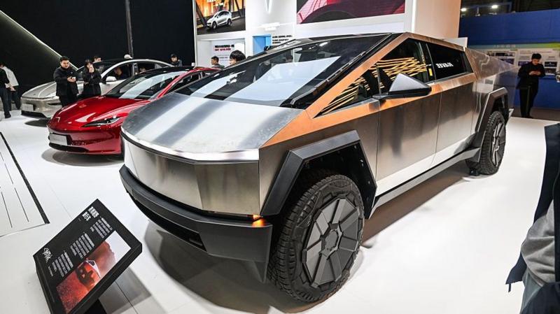 A series of Tesla electric cars on a show floor, including the angular Cybertruck in the foreground.