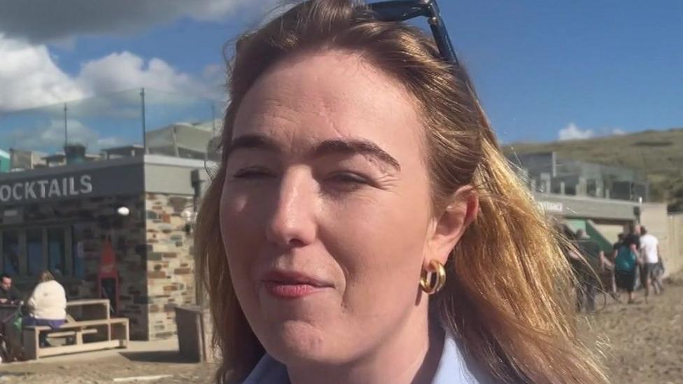 A woman called Jamie-Lee Job. She appears to be squinting. She has shoulder-length brown hair which has blonde highlights in it. Her sunglasses are propped on top of her head. She has make up on.
