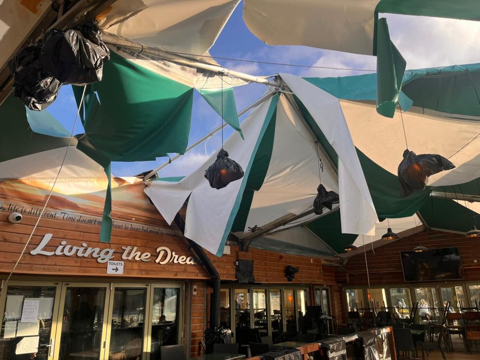 A green and white roof canopy that has been shredded by bad weather