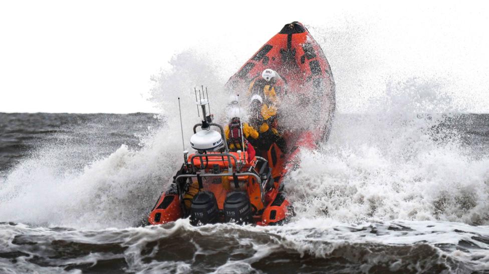 A motor-powered boat is pictured crashing through waves away from the shore, with three people tucked down as the boat elevates.