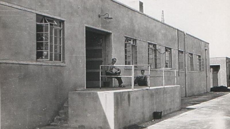 Two men lounge on a raised concrete platform attached to a long, rectangular building.