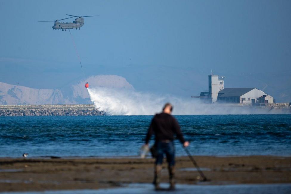 A Chinook helicopter practices picking up and dropping water from a fire fighting water bucket in Portland harbour.