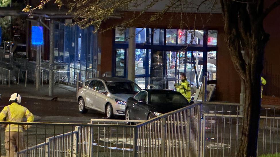 An entrance to a supermarket with two cars and police outside