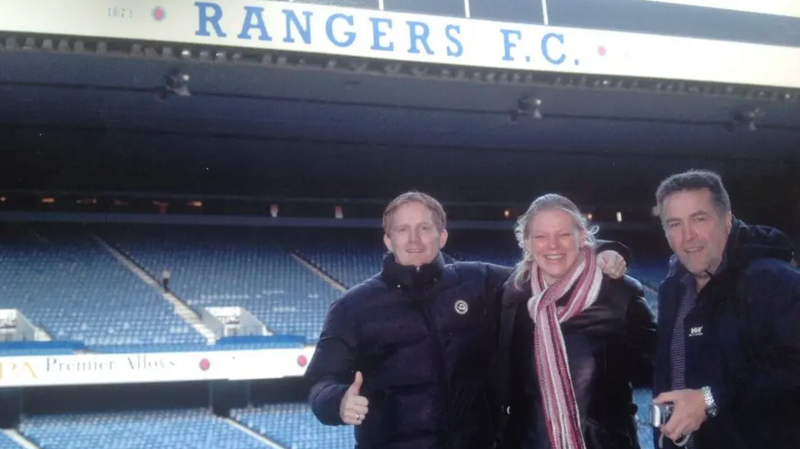 Dennis van Unen wearing a black jacket and standing in front of the main stand at Ibrox.