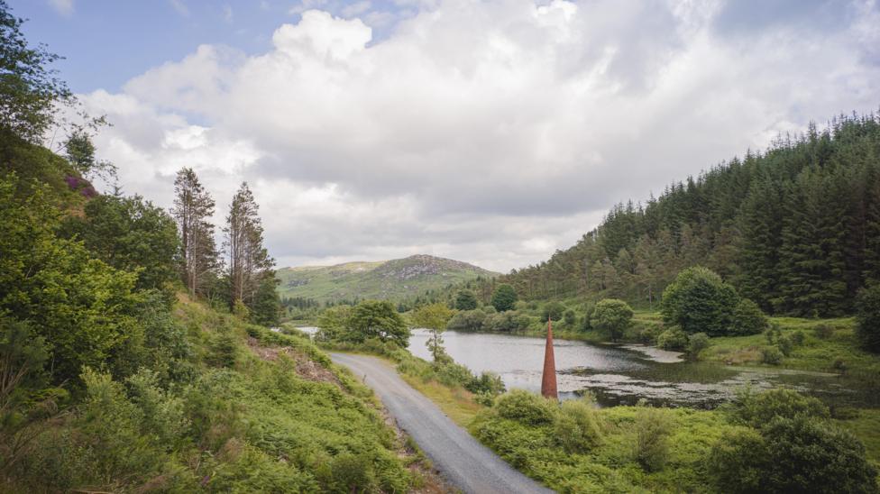 A loch surrounded by tree-lined hills and a road