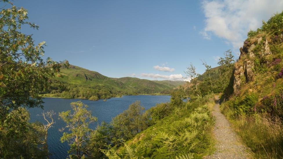 A loch side walk with trees and hills in the distance