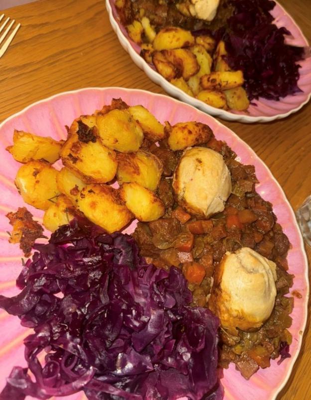 A pink plate with roast potatoes, meat and carrot stew, dumplings and red cabbage