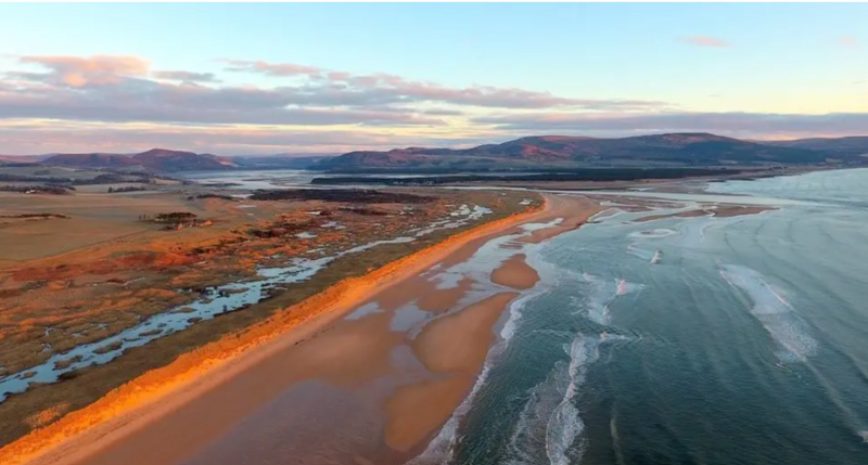 An area of beach with orange sands and hills in the background