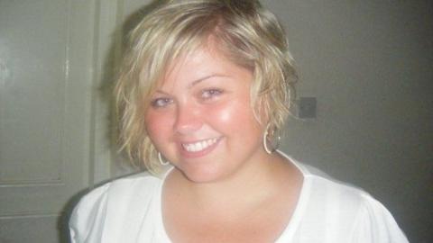 Hayley, wearing a white top, as a younger woman. She is smiling broadly at the camera and is wearing hoop earrings. 