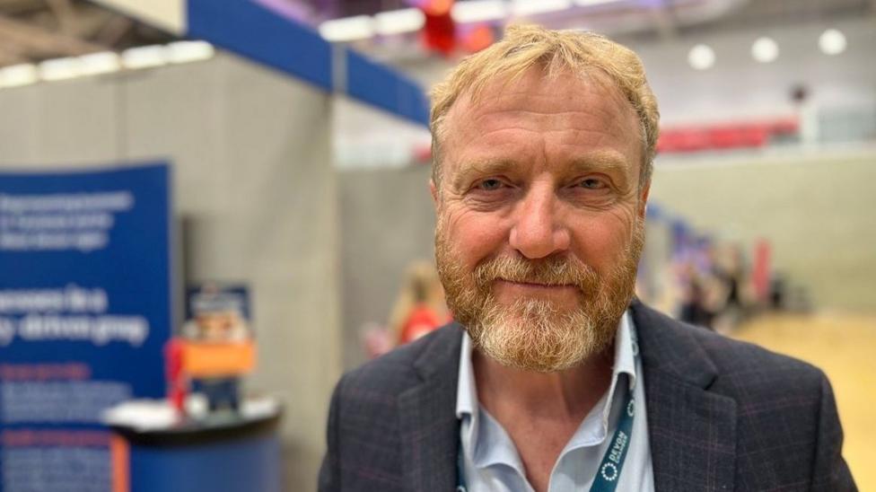 Tim Randell in a blue shirt and a dark check jacket and a Devon Chamber lanyard