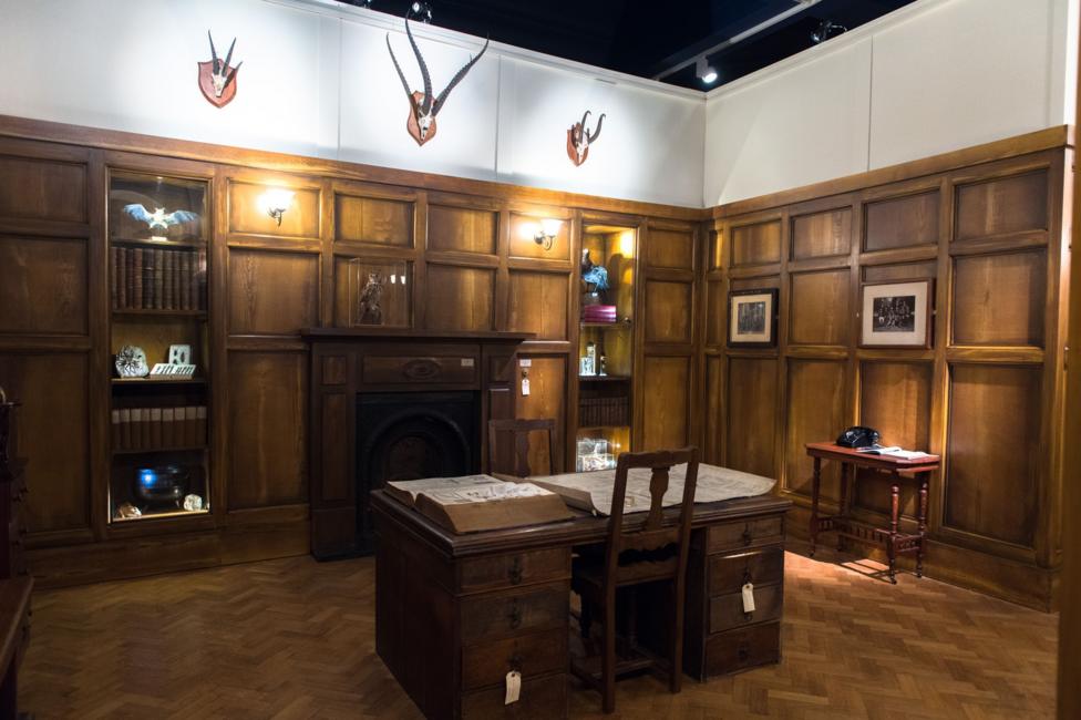 There is a wooden desk with a chair in a wood panelled space.