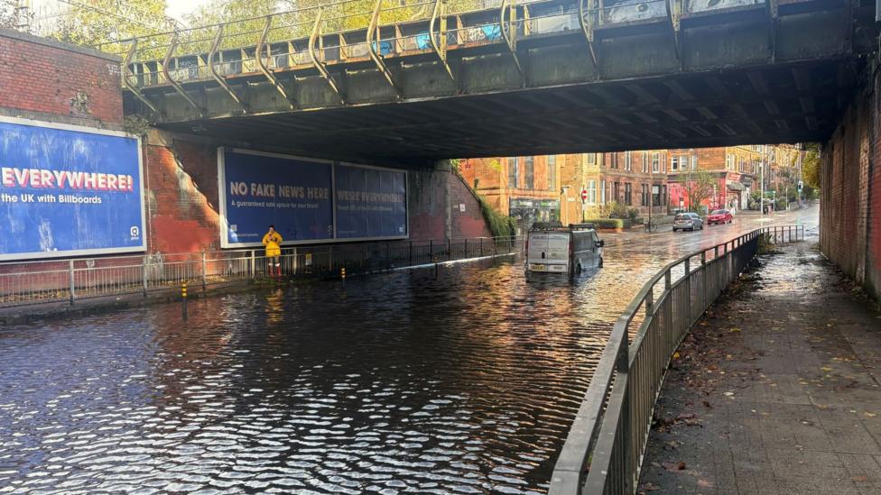 Flood water covers the road where it goes under a bridge.