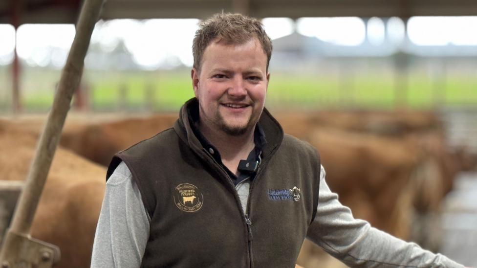 Caleb smiling at the camera, he is wearing a brown bodywarmer and grey long sleeve top.