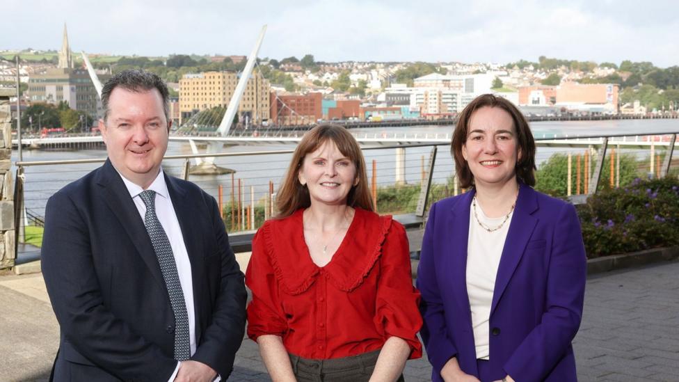 Aeidin McCarter, head of regional business for the north west, pictured in a purple suit jacket with Kieran Donoghue, chief executive of Invest NI and Economy Minister Dr Caoimhe Archibald.