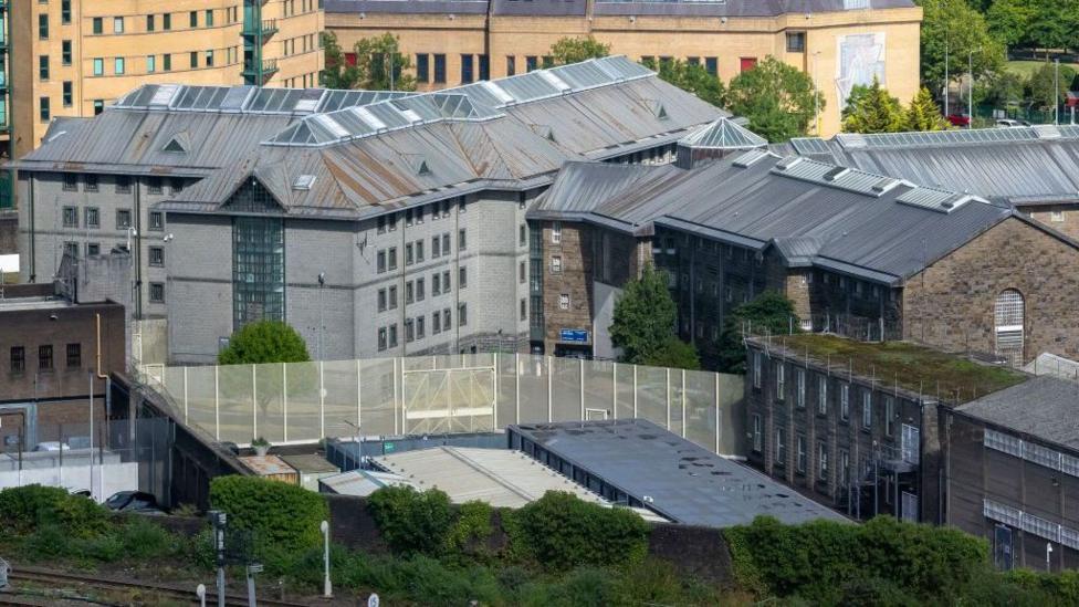 A view of HMP Cardiff, with a group of buildings in the middle of the picture, and a fence viewable from the front.