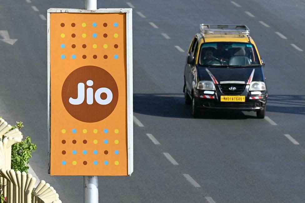 A black and yellow Mumbai taxi rides past a Jio advertisement in Mumbai.