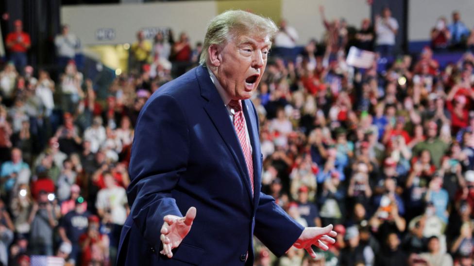 US President Donald Trump at a rally in support of Republican US Senate reelection candidate Roger Marshall in Kansas on 19 October. He wears a blue suit, white shirt and red and white patterned tie