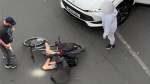 A man standing over a cyclist who is lying on the road with his face blurred.