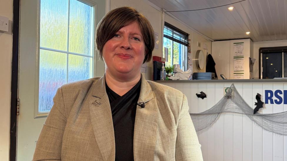 A woman with a short brown bob looks at the camera with an RSPCA sign and black plastic bats and the reception desk behind her. 
