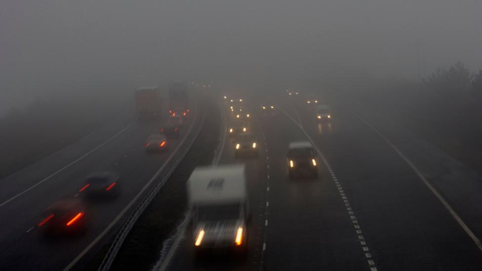 Photograph of vehicles including cars and vans on a dual carriageway road with their headlights on in foggy conditions. Other cars are attempting to join the road from a slip road.