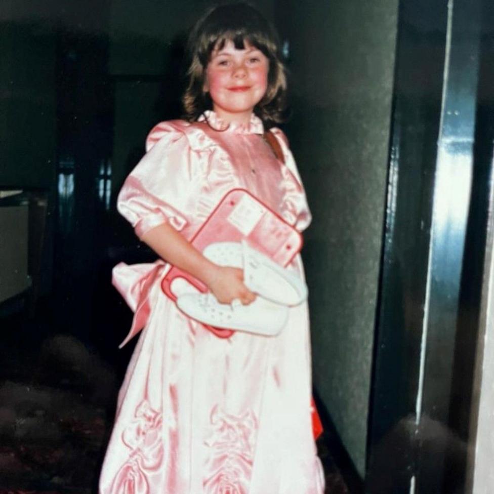 Clare as a child wearing a light pink flower girl dress