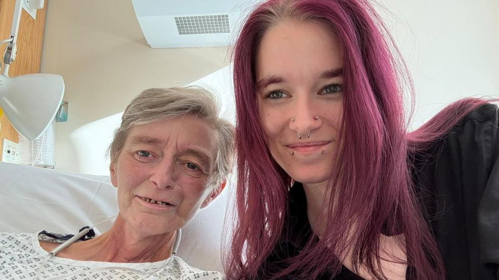 Rachael and her daughter Kyra at the hospital. Racheal has short grey hair, Kyra has long hair and piercings on her face.