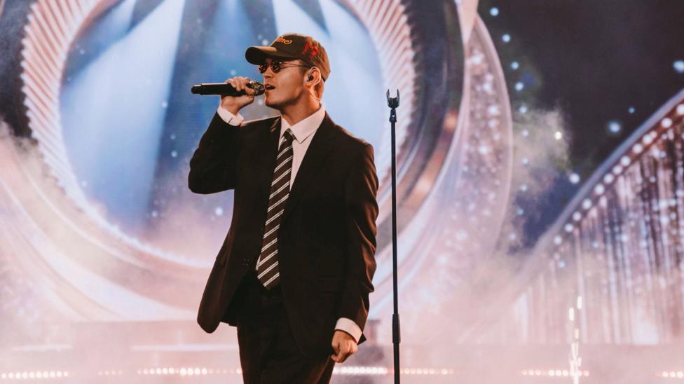 Jamie Miller wearing a suit on stage holding a microphone.