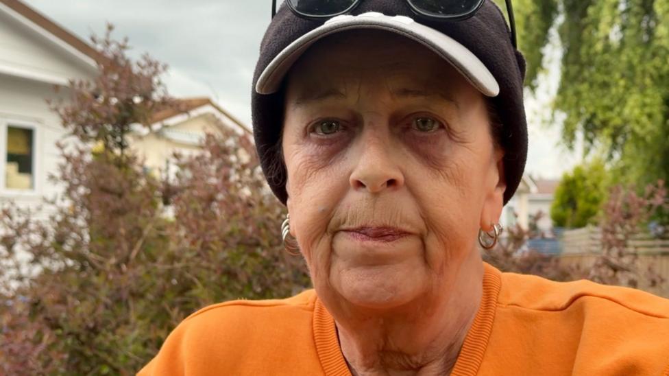Leigh Radwell looking towards the camera is wearing orange and a black hat.
