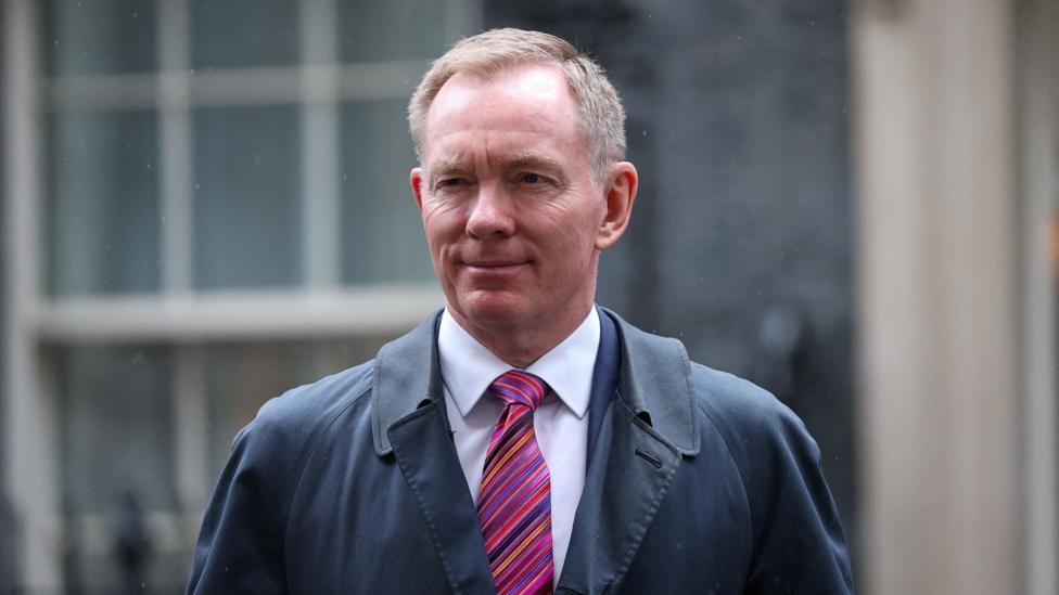 Northern Ireland Secretary Chris Bryant - a man with short, greying fair hair, smiles as he walks on Downing Street in London. He is wearing a pale shirt, a pink tie with multicoloured diagonal stripes and a navy overcoat. The photo was take in early September. 