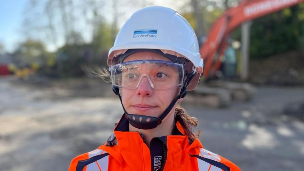 A woman wearing a white protective helmet and orange fluorescent jacket.