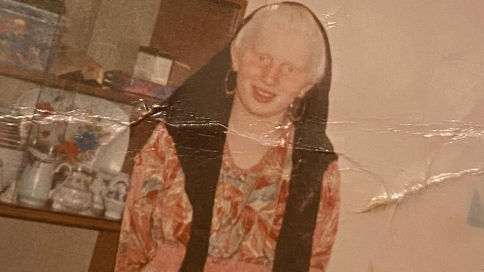 An old photo of Naseem when she was younger, she is wearing a dress with various colours and hsa a black scarf draped over part of her head.