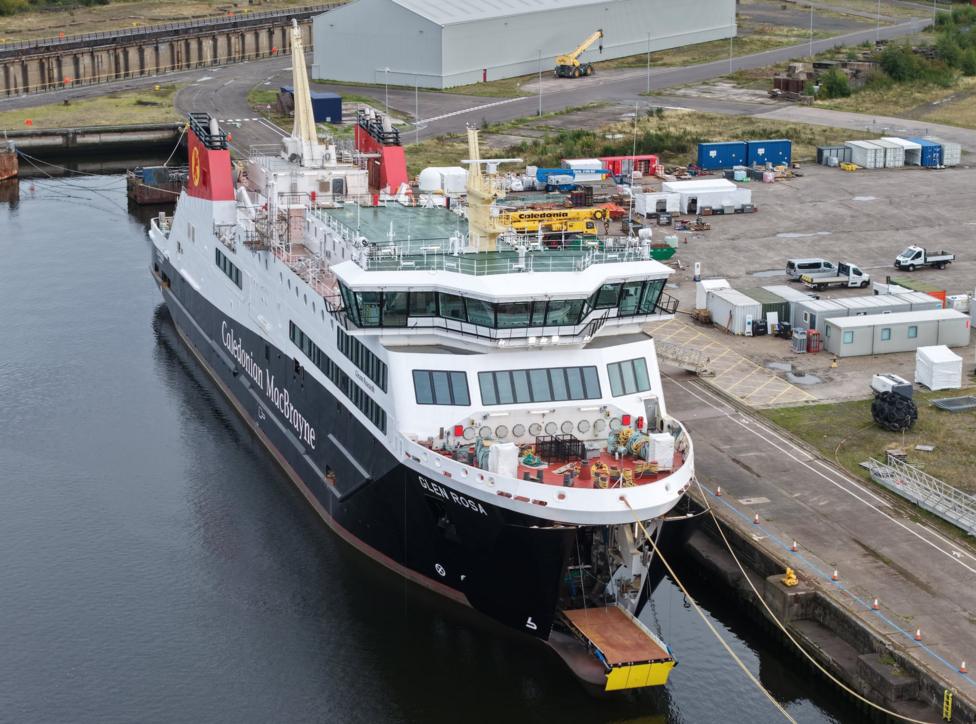 A large black and white ship with red funnels, moored at a quayside