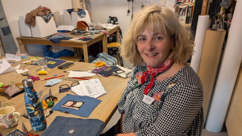 Lisa sitting at a bench with sewing projects on it.