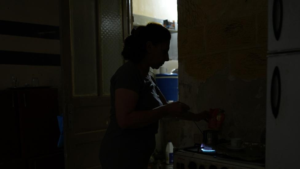 Profile of a woman heating up water on a stove standing in near darkness