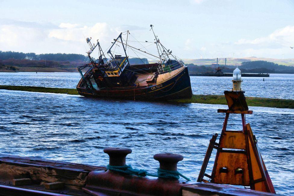 A fishing boat washed up near land after a storm.