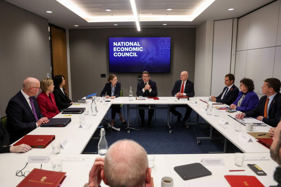 A group of officials sitting round a white desk with a TV screen in the background which reads "National Economic Council"
