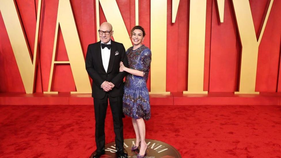 Patrick Stewart and wife Sunny Ozell stood on a red carpet with large gold letters which spell out 'Vanity'