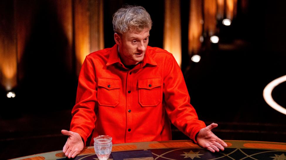 James Acaster speaking at the round table with both palms outstretched