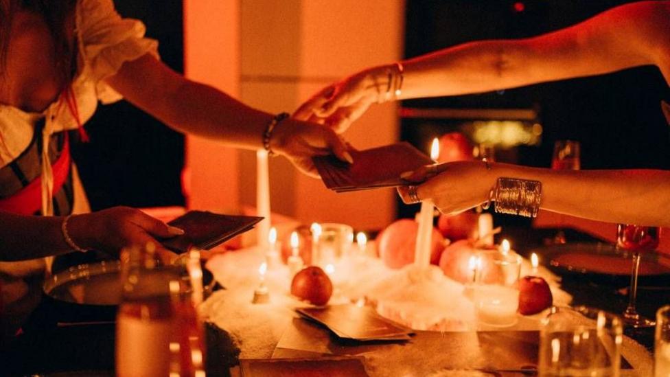 Hands passing tarots cards over a table filled with candles