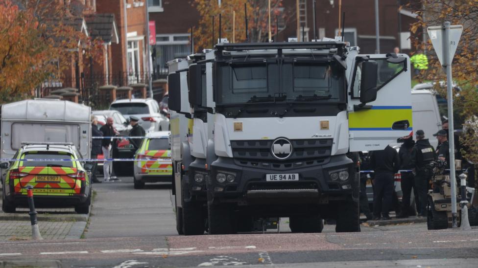 Two large white lorries and two police cars at the scene of the searches in west Belfast.